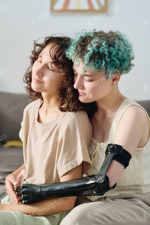 Preview: Young female amputee with short blue curly hair embracing her girlfriend