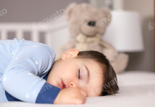 Preview: Close up portrait of cute little baby boy in light blue pajamas sleeping peacefully on bed at home