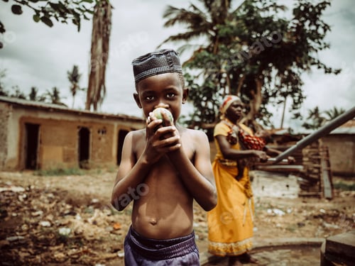 Preview: Young Mozambican boy in a traditional hat eating a fruit.