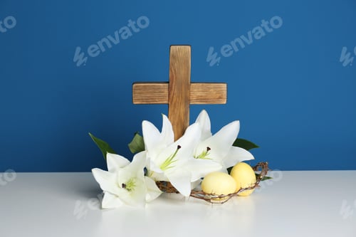 Preview: Wooden cross, crown of thorns, Easter eggs and blossom lilies on table against color background