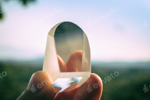 Preview: Crystal prism in hand between fingers agains sky