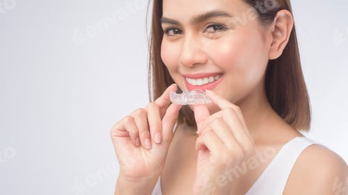 Preview: Young smiling woman holding invisalign braces over white background studio,