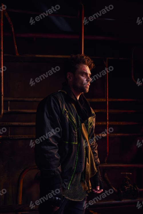 Preview: unshaven man in black jacket looking away near rusty pipes in post-disaster underground tunnel
