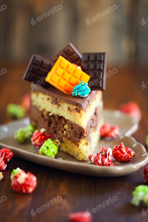 Preview: Piece of dark chocolate cake decorated with chocolate bars and pop corn on the plate