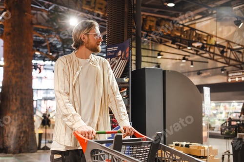 Preview: Young stylish man pushing shopping cart in grocery store