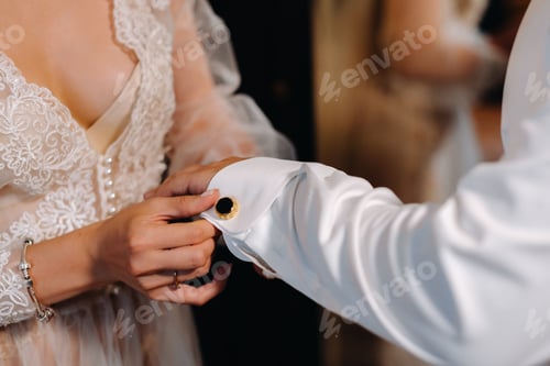 Preview: Close-up of the bride in boudoir underwear buttoning cufflinks on her sleeve
