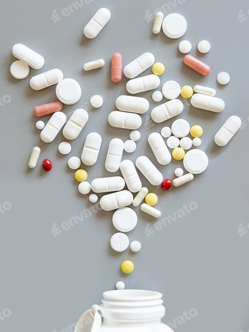 Preview: Mix of medical capsules and pills fall out of a bottle on grey top view. Medicinal treatment
