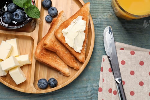 Preview: Tasty toasts served with butter and blueberries on light blue wooden table, flat lay
