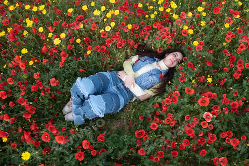 Preview: Young happy girl resting in the field of red poppy flowers. Drone scenery of woman in spring