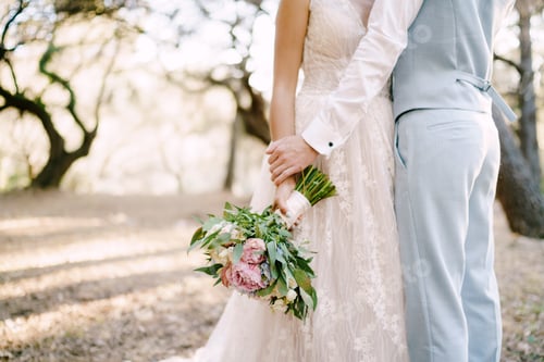 Preview: The bride and groom are embracing among the trees, the bride holds bridal bouquet, close-up