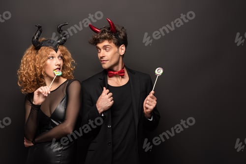 Preview: beautiful couple posing in halloween costumes with sweet lollipops on black