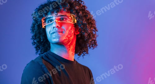 Preview: Young beautiful man with curly hair is indoors in the studio with neon lighting