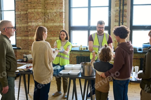 Preview: Several refugees standing by table with cooked food in front of volunteers