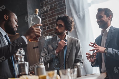Preview: low angle view of young multiethnic businessmen smoking cigars and drinking whisky