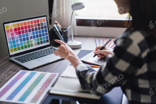 Preview: Female artist designer choosing color swatch samples on laptop and drawing logo on graphic tablet