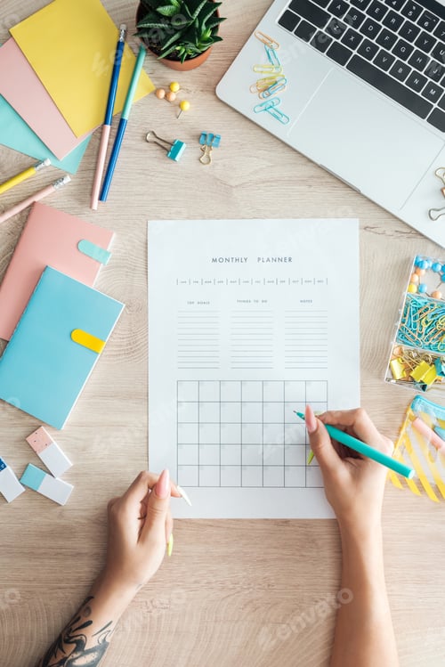 Preview: cropped view of woman sitting behind wooden table with laptop and stationery, writing notes in