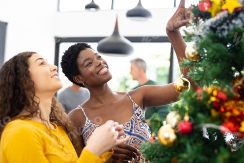 Preview: Happy diverse female friends decorating christmas tree at christmas