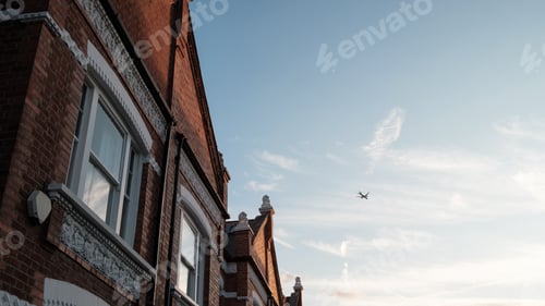 Preview: Airplane flying over typical english terraced houses in london suburb at sunset