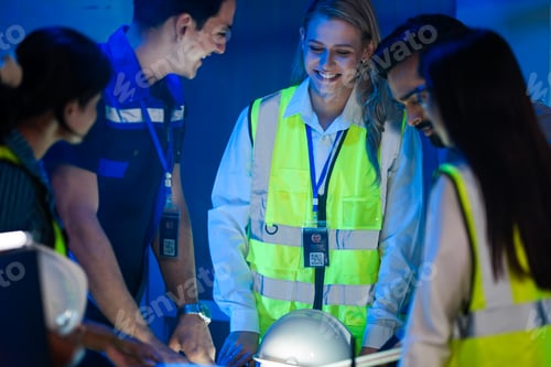 Preview: A happy, diverse team of engineers in safety vests collaborates at night.