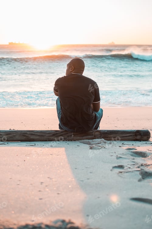 Preview: A shot from the back of a young man sitting on the beach at sunset