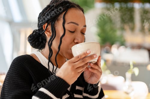 Preview: Young woman enjoying warm drink in cafe