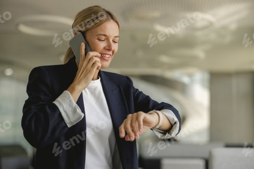 Preview: Female sales manager looking at wristwatch to checking time while having a phone call with client