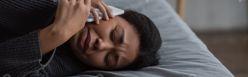 Preview: Upset multiracial woman talking on smartphone while lying on bed at home, banner