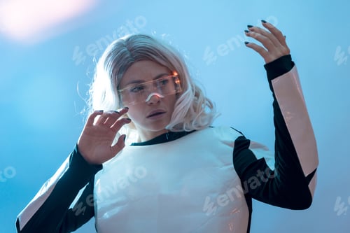 Preview: Woman looking through the illuminated futuristic glasses, virtual reality on a blue background