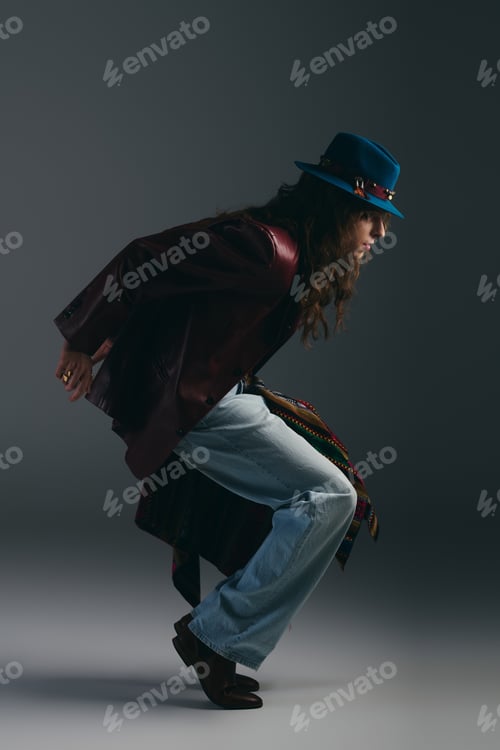 Preview: Stylish young man in a dramatic pose wearing a hat and a fashionable outfit indoors