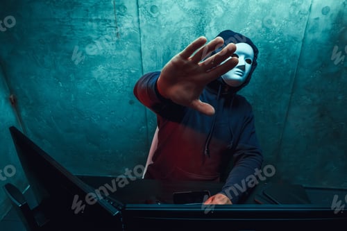 Preview: Anonymous hacker wearing face mask working on computer in dark room