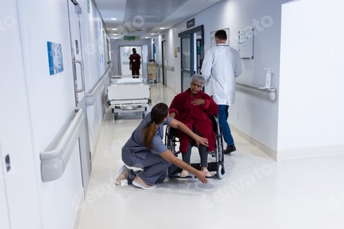 Preview: Asian female doctor checking leg of diverse senior female patient in wheelchair in hospital corridor
