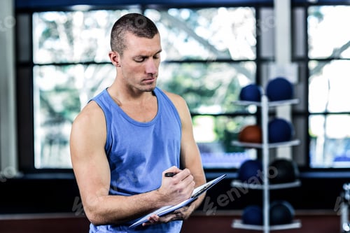 Preview: Clipboard and pen leaning against rack of colorful medicine balls near gym windows