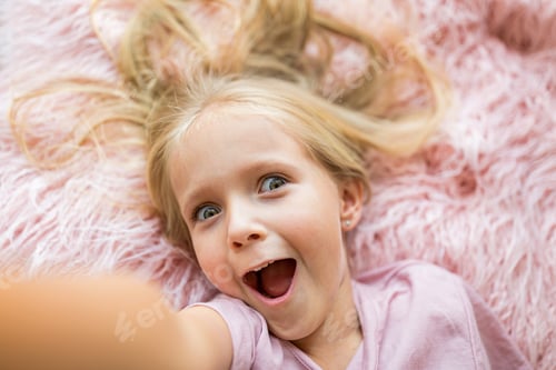 Preview: Happy little Caucasian girl with blonde hair making selfie on pink background