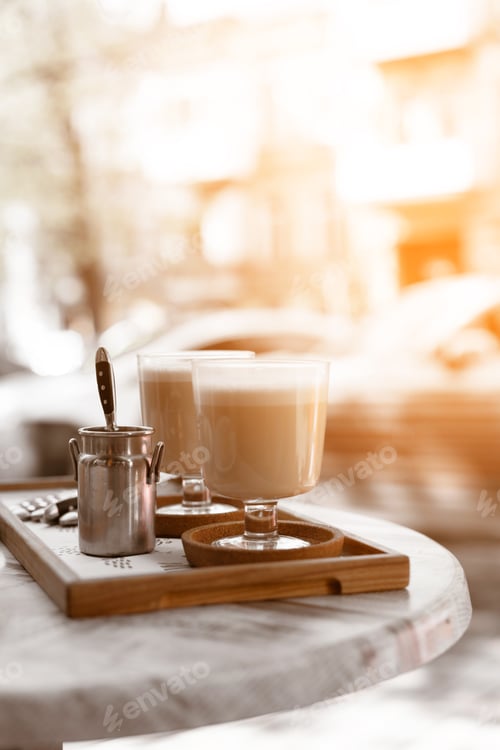 Preview: Aromatic latte coffee in a glass mug on a coffee table in a street restaurant. Tasty morning drinks.