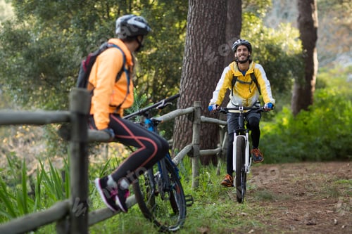 Preview: Male Biker Cycling While Female Biker Sitting On A Fence In Countryside