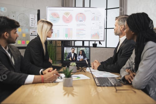 Preview: Focused multiracial business people in conference room, looking at a laptop, having video conference