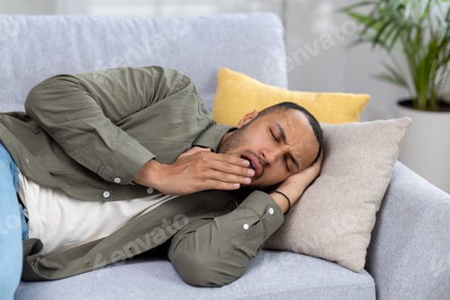 Preview: Close-up photo of tired young hispanic man resting and sleeping on sofa at home, yawning and