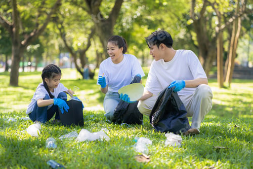 Preview: Asian family collects plastic bottles into black bags at a park on the weekend.
