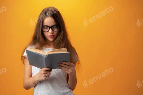 Preview: Smart teen girl in glasses holding book against yellow background