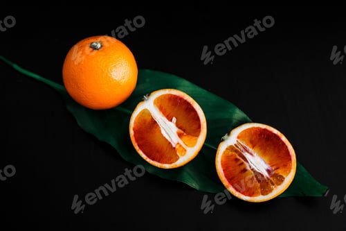 Preview: 3 red oranges on a black background decorated with green leaves