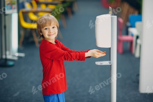 Preview: Child smiling boy kid using automatic alcohol gel dispenser spraying on hands sanitizer machine