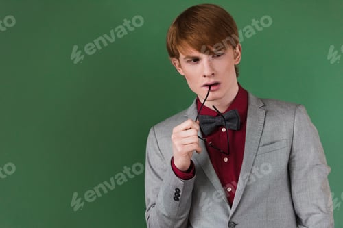 Preview: Male fashion model holding eyeglasses near lips isolated on green