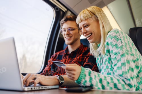 Preview: Cheerful travelers in train using laptop and credit card during trip.