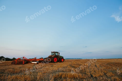 Preview: Modern tractor with a heavy trailed disc harrow works a wide hilly field.