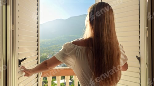 Preview: Young woman in a long dress gracefully opens balcony doors, steps onto the terrace
