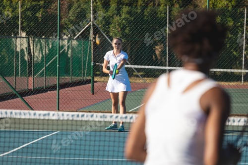 Preview: Caucasian female player serving tennis ball to competitor at court on sunny day
