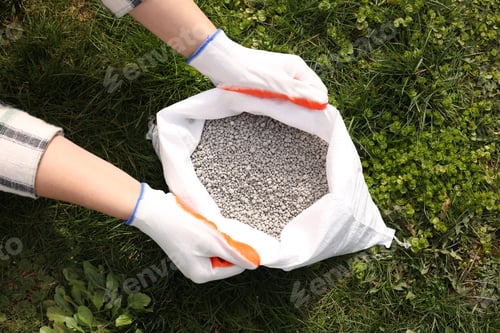 Preview: Woman with bag of fertilizer on green grass outdoors, top view
