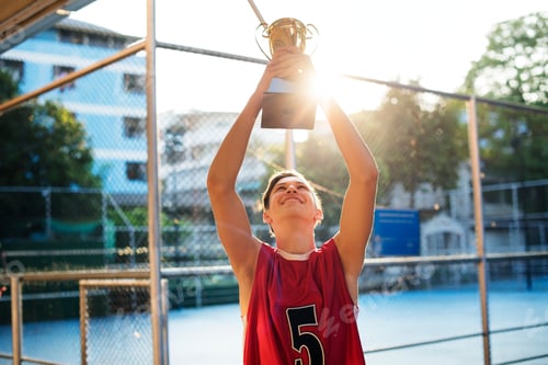 Preview: Caucasian teenage boy in sporty clothes holding up a trophy outdoors