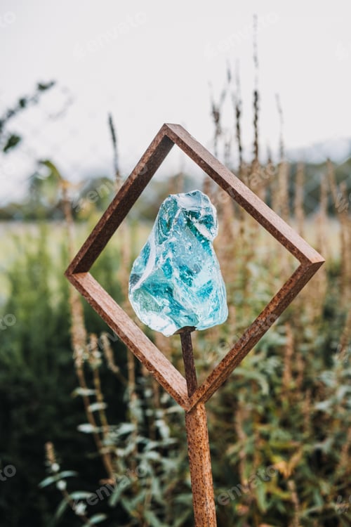 Preview: Aqua-colored glass sculpture held within a rusty iron frame displayed in a garden setting.