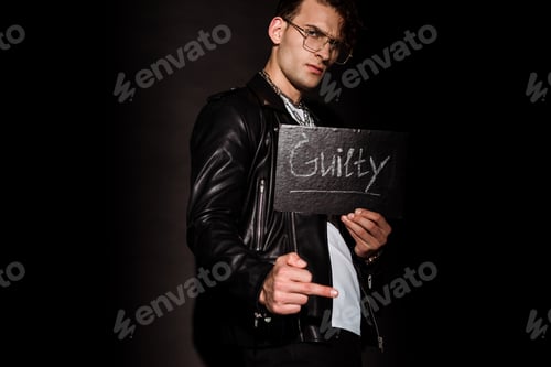 Preview: handsome man in glasses holding chalk board with guilty lettering on black